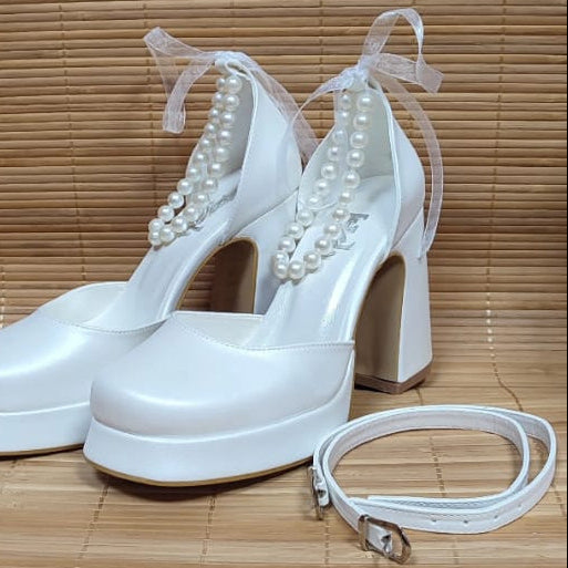 White high-heeled shoes with pearl embellishments on a wooden surface