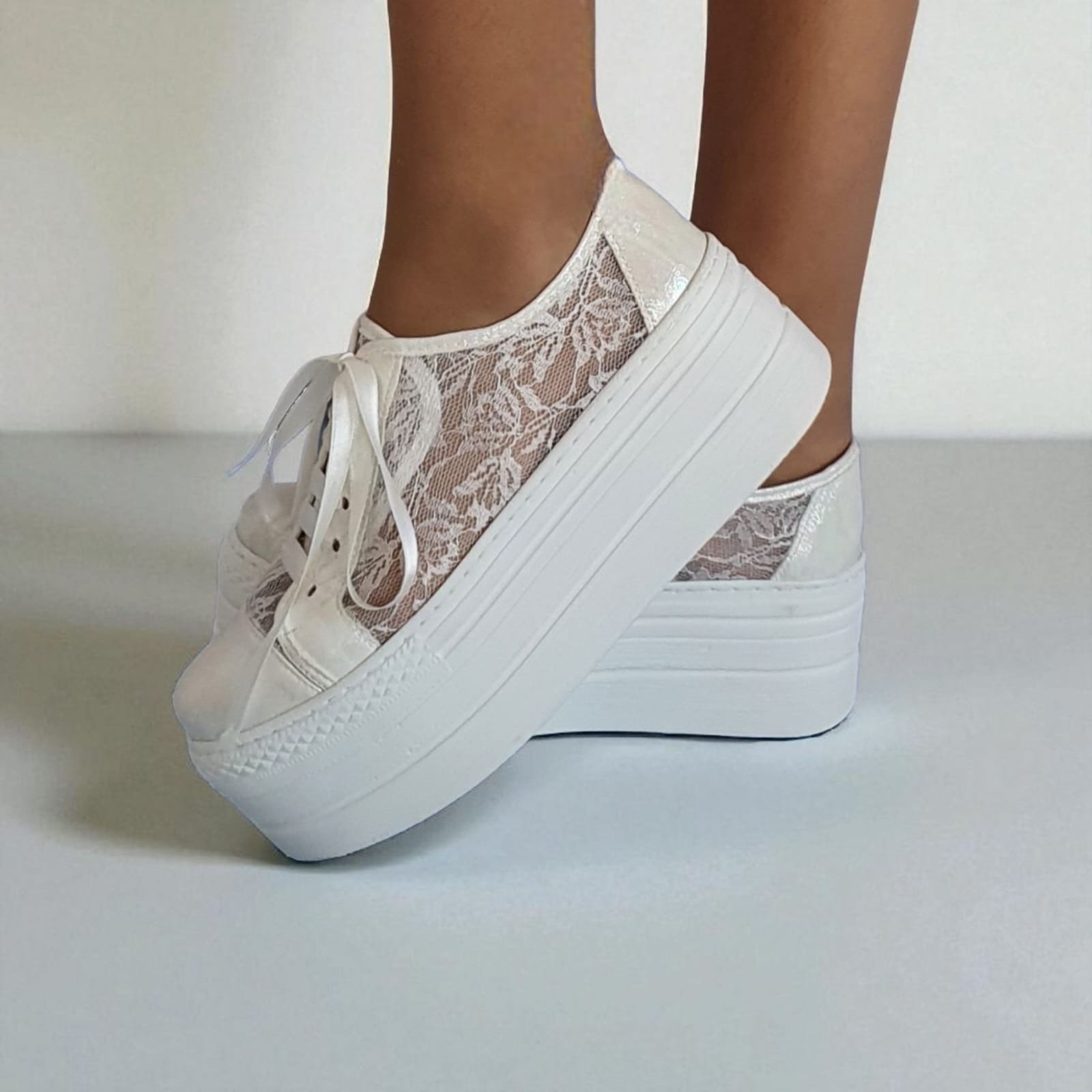 White platform sneakers with lace details worn by a person on a light background