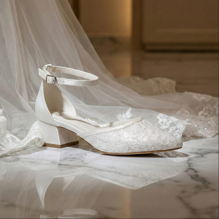 Comfortable low heel wedding shoes for brides with secure ankle buckle and soft lace upper on a marble floor.